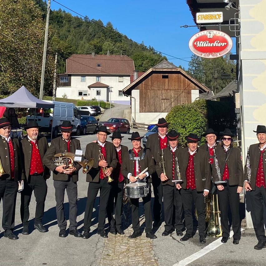 Eine Gruppe von Musikern in traditioneller Kleidung posiert für ein Foto vor einem Gebäude mit einem Schild, das 'Villacher' liest.