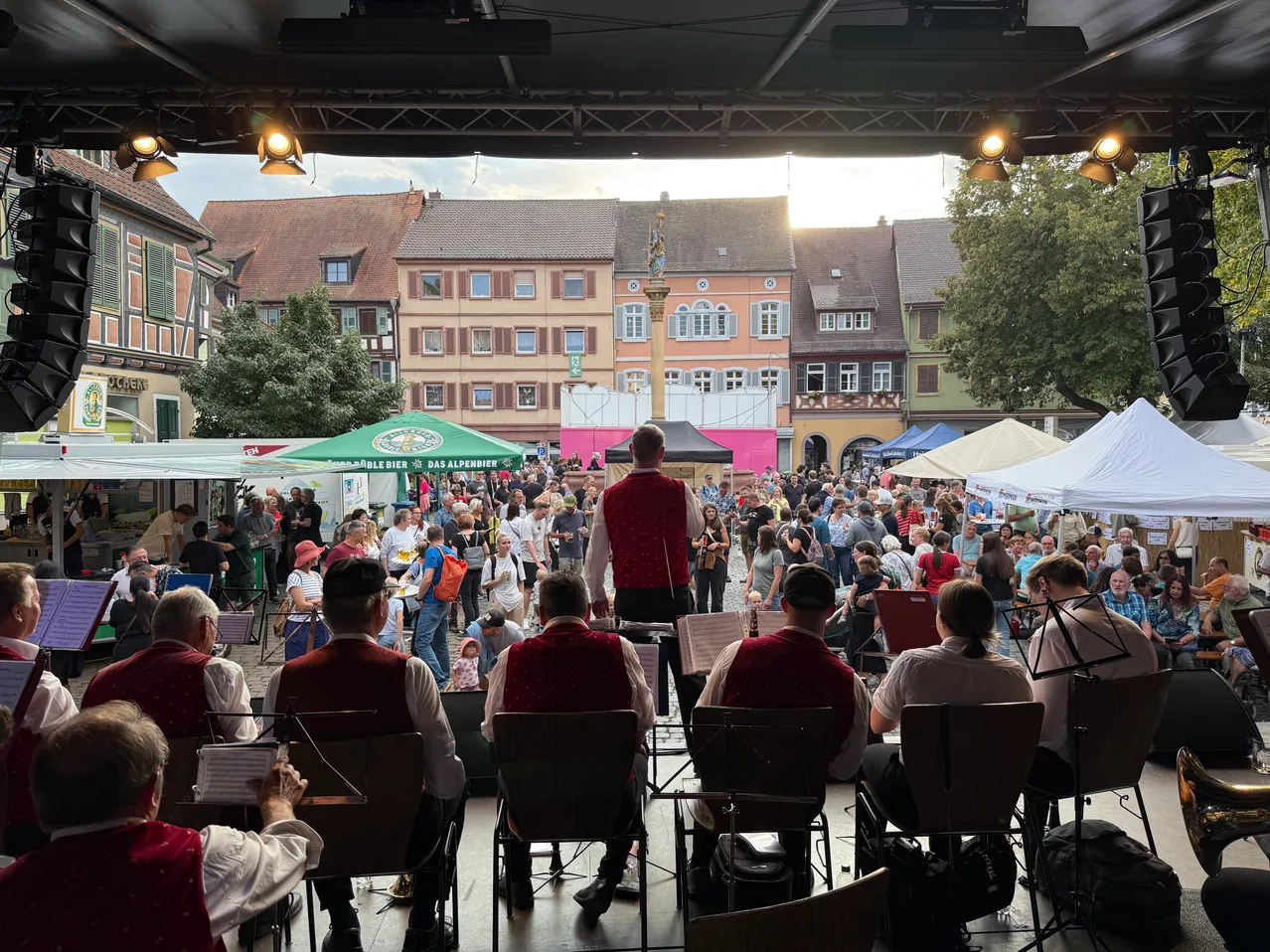 Eine Band spielt auf einer Bühne vor einer großen Menschenmenge im Freien.