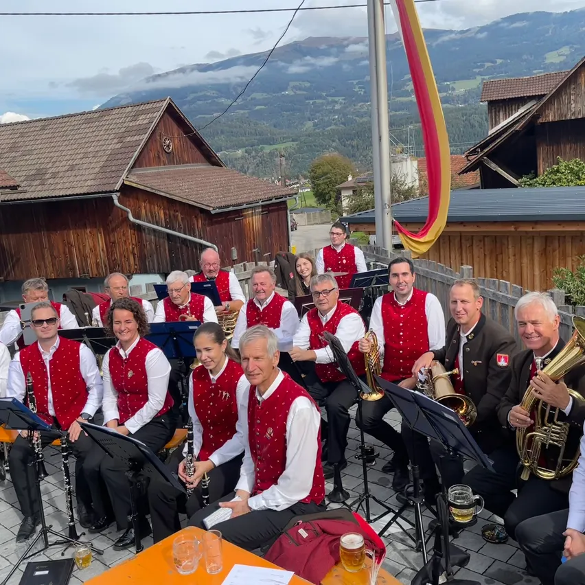 Eine Gruppe von Musikern, die rote Westen und weiße Hemden tragen, sitzen auf einer Bühne mit Musikinstrumenten, möglicherweise für eine Aufführung.