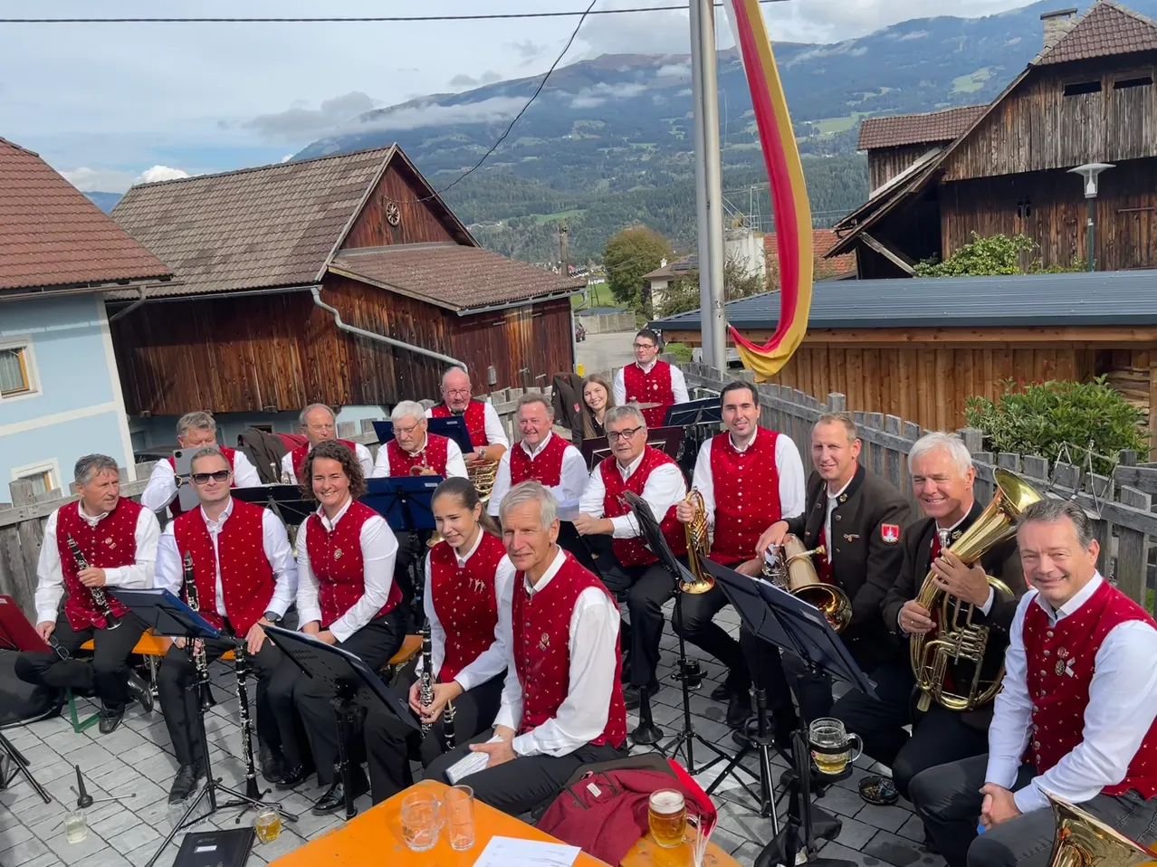 Eine Gruppe von Musikern, die rote Westen und weiße Hemden tragen, sitzen auf einer Bühne mit Musikinstrumenten, möglicherweise für eine Aufführung.