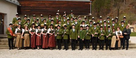 Eine große Gruppe von Menschen in grünen Uniformen posiert für ein Foto und hält Musikinstrumente. Sie stehen auf Betonstufen vor einem Gebäude.