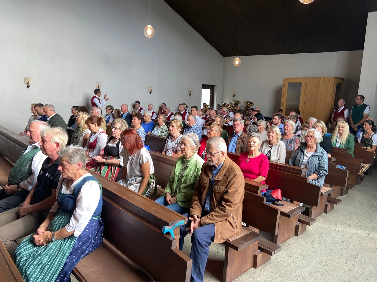 Eine große Gruppe von Menschen, hauptsächlich ältere Personen, sitzt in einer Kirche. Einige tragen traditionelle Kleidung. Ein Mann steht vorne, möglicherweise leitet er einen Gottesdienst.