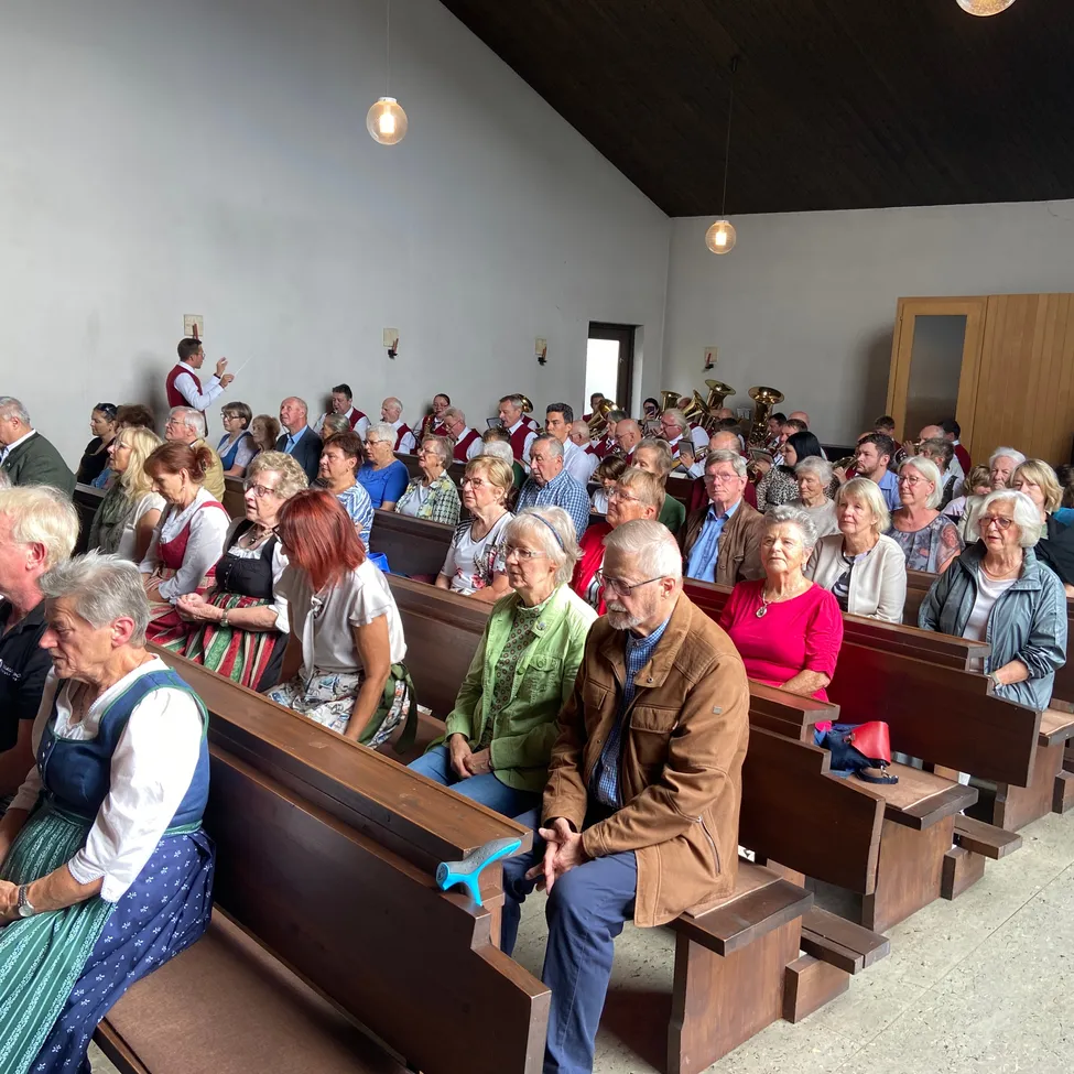Eine große Gruppe von Menschen, hauptsächlich ältere Personen, sitzt in einer Kirche. Einige tragen traditionelle Kleidung. Ein Mann steht vorne, möglicherweise leitet er einen Gottesdienst.