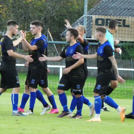 Eine Gruppe von Fußballspielern in blauen und schwarzen Trikots feiert auf dem Spielfeld in der Nähe eines Zauns mit einem Schild, das OPEL steht.