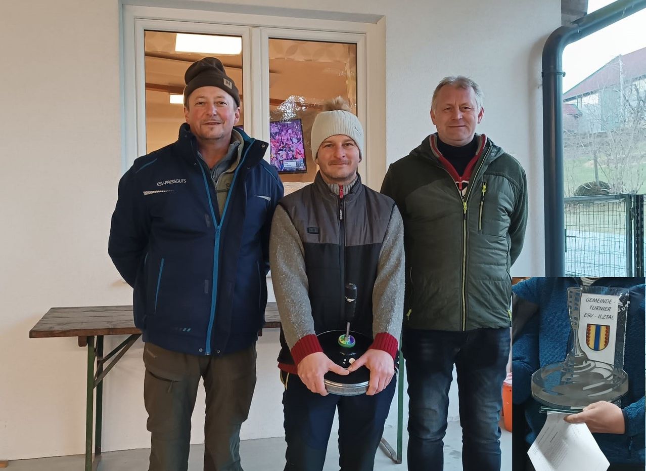 Drei Männer stehen nebeneinander vor einer Glastür und lächeln für ein Foto. Der Mann in der Mitte hält einen Pokal.