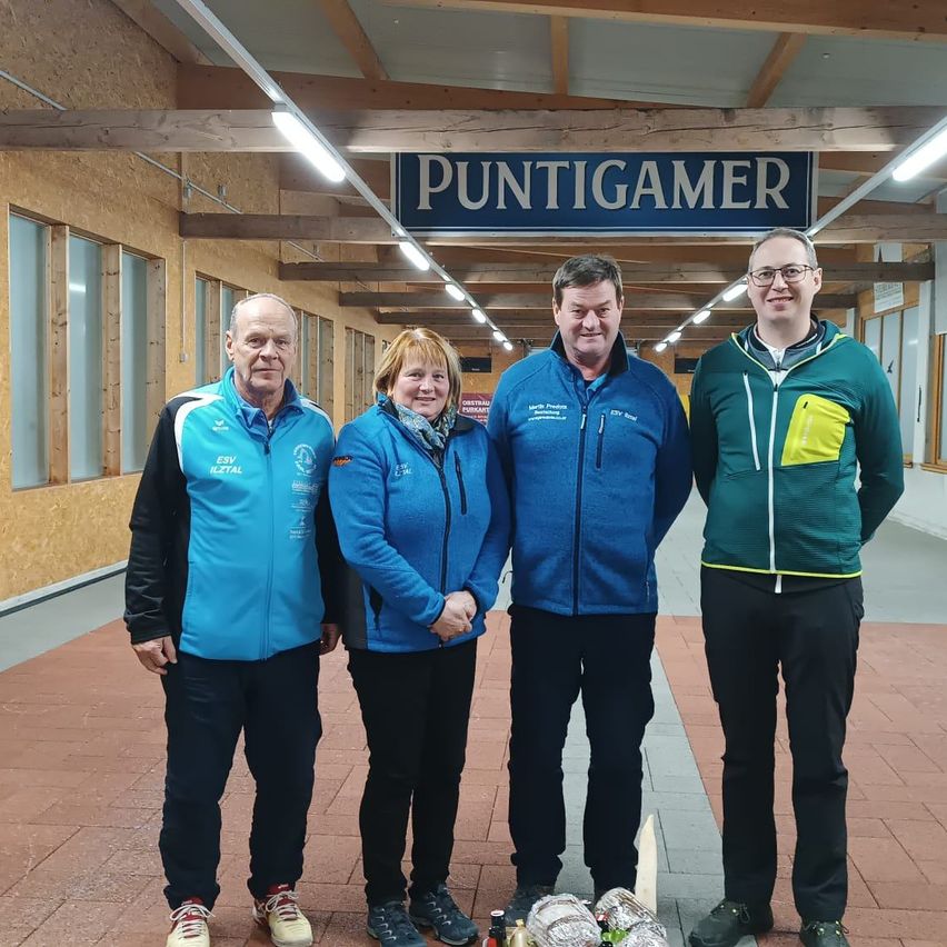 Vier Menschen stehen vor einem Gebäude und lächeln. Sie tragen Jacken, Hosen und Turnschuhe. Ein Schild sagt 'Puntigamer'.