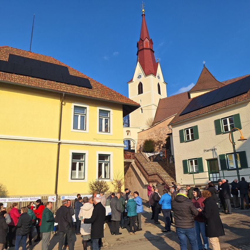 A group of people are standing in front of buildings with solar panels on the roofs, under a clear blue sky.