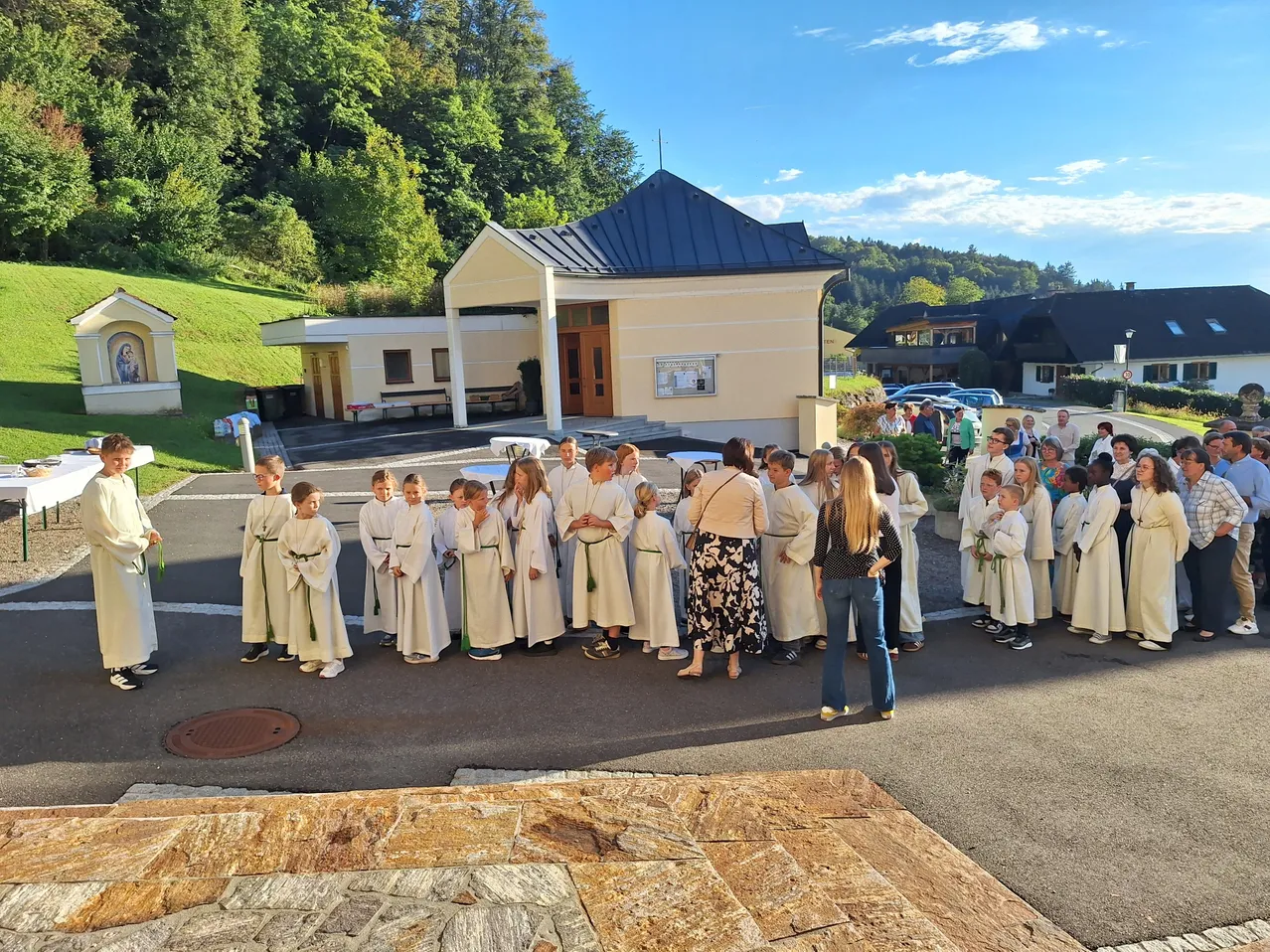 Eine Gruppe von Kindern in weißen Gewändern steht an einem sonnigen Tag vor einer Kirche.