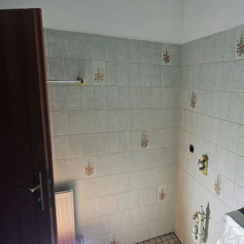 An empty shower stall with white tiles, a showerhead, a faucet, and a wooden door.