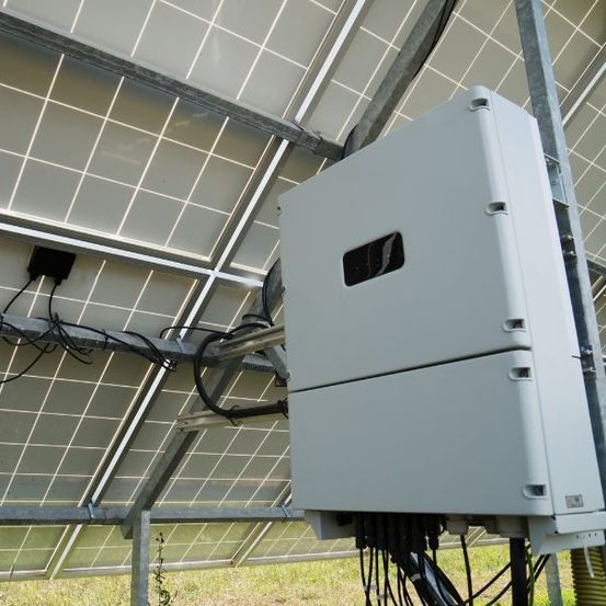 Ein Solarstromsystem mit Paneelen und einem Wechselrichter, montiert auf einer Metallstruktur, unter einem hellen Himmel.