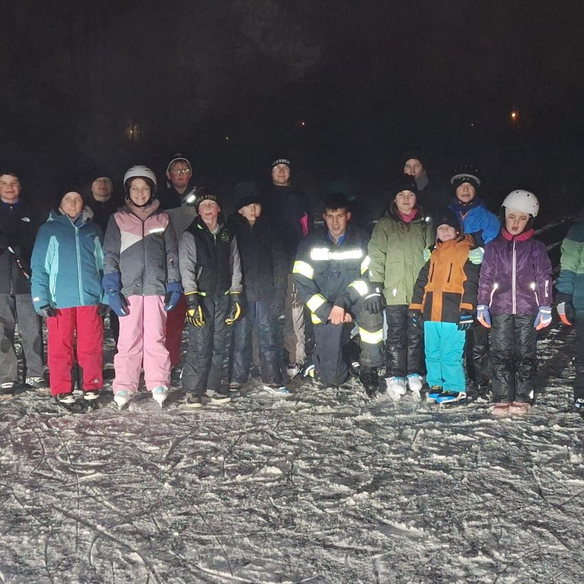 Eine Gruppe junger Leute in Winterkleidung steht bei Nacht auf einem verschneiten Feld und posiert lächelnd für ein Foto.