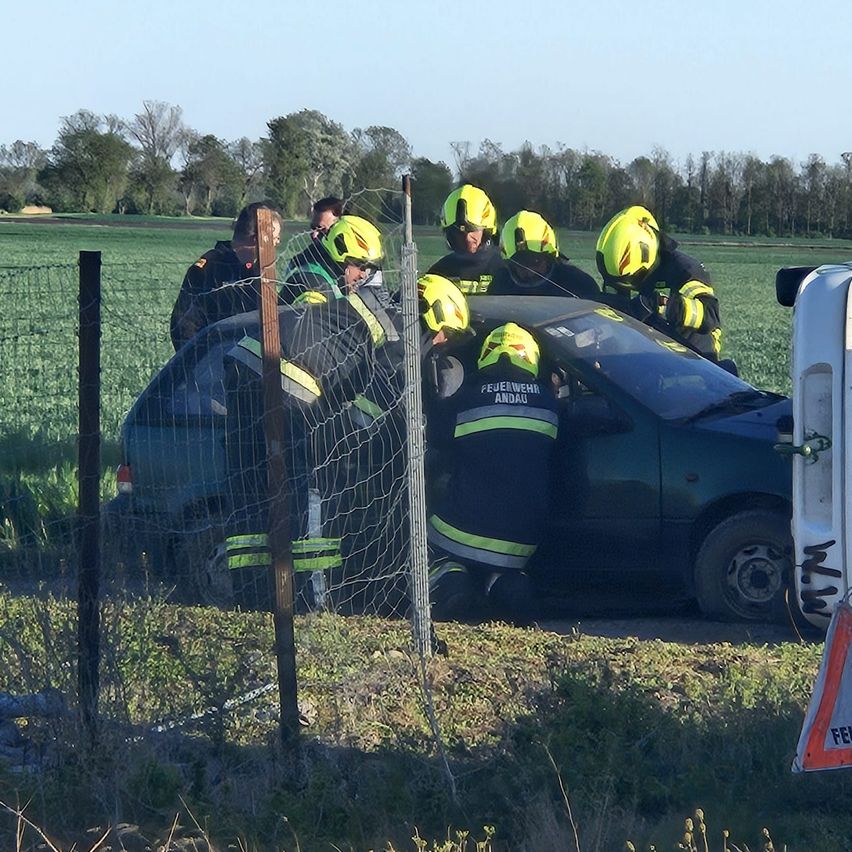 Feuerwehrleute in Schutzkleidung arbeiten an einem Autounfall auf einem ländlichen Feld.