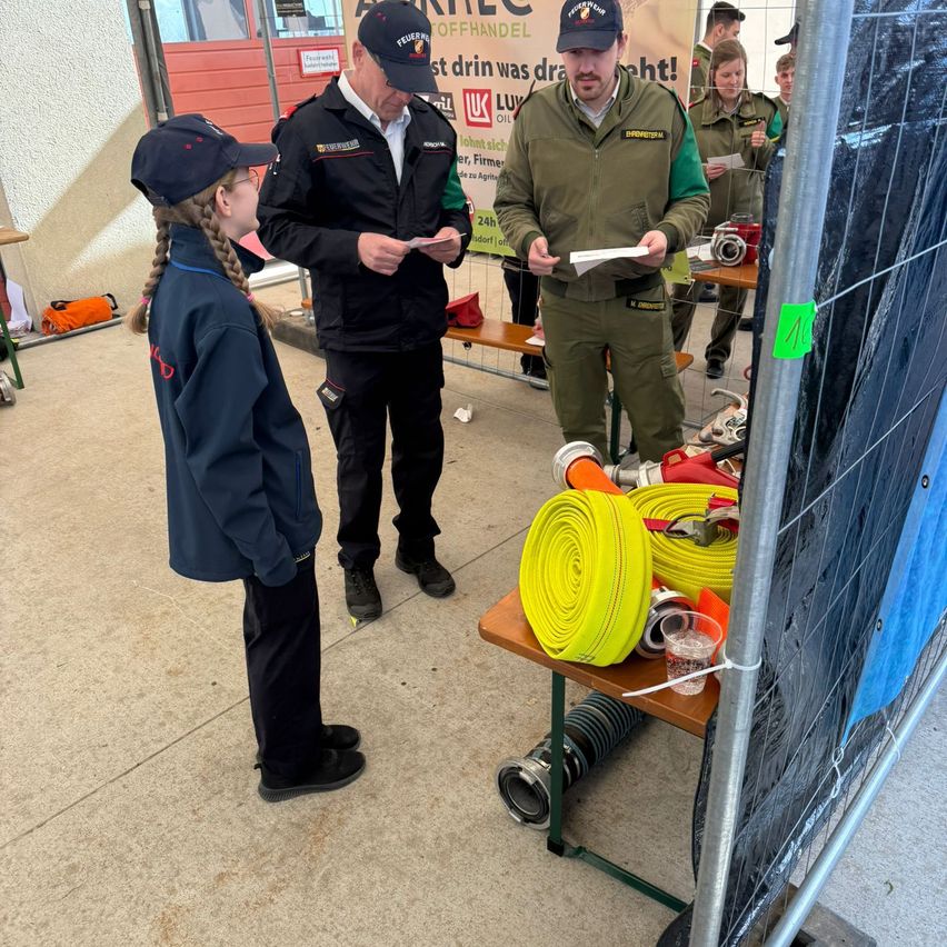 Eine Gruppe von Feuerwehrleuten führt eine Schulung durch. Ein Mann und ein junges Mädchen stehen vor einem Tisch mit Ausrüstung.