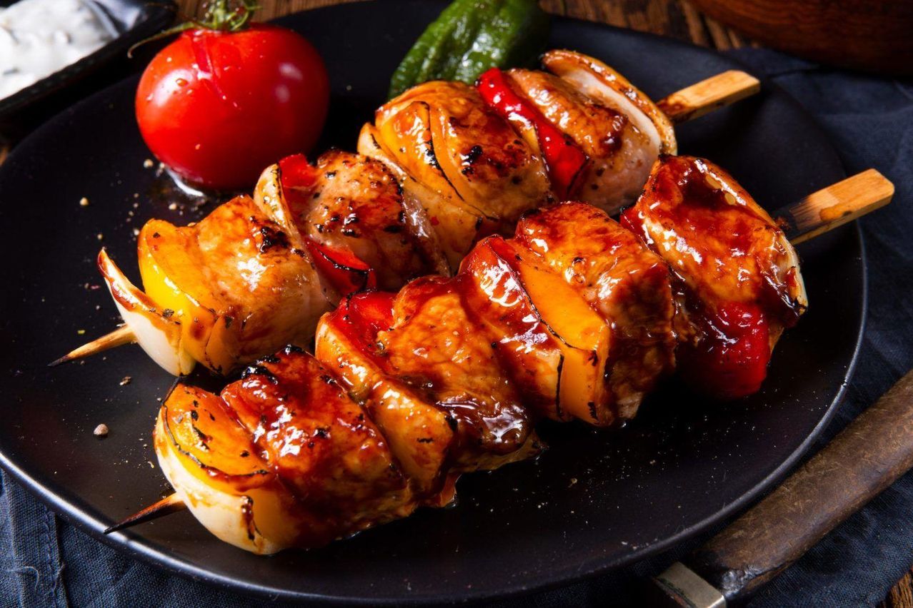 Ein schwarzer Teller mit Hähnchenspießen und Gemüse auf einem Holzuntergrund.