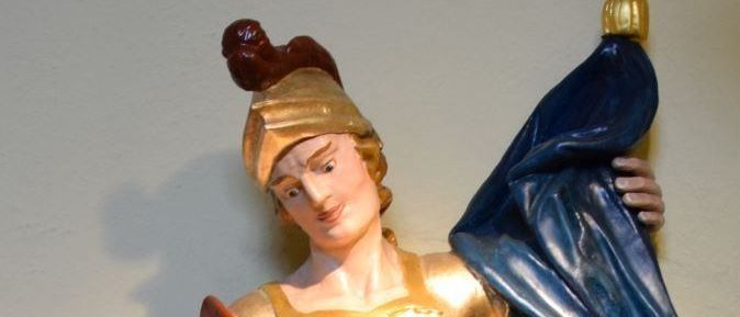 Eine goldene Statue einer Frau, die einen Becher hält und einen blauen Umhang, einen roten Umhang und einen grünen Rock trägt.