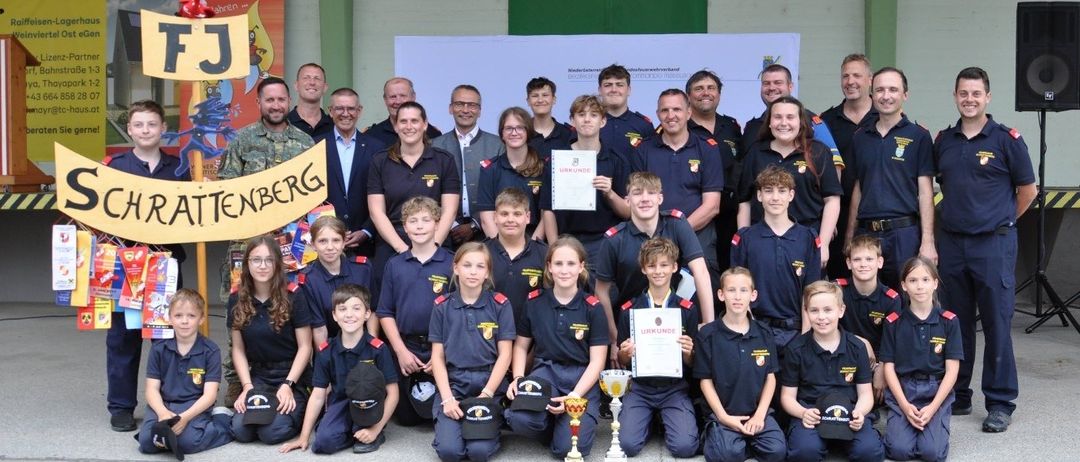 Eine Gruppe junger Menschen in blauen Uniformen mit einigen Erwachsenen posiert für ein Foto mit Trophäen und Urkunden. Sie stehen auf einer Betonfläche.