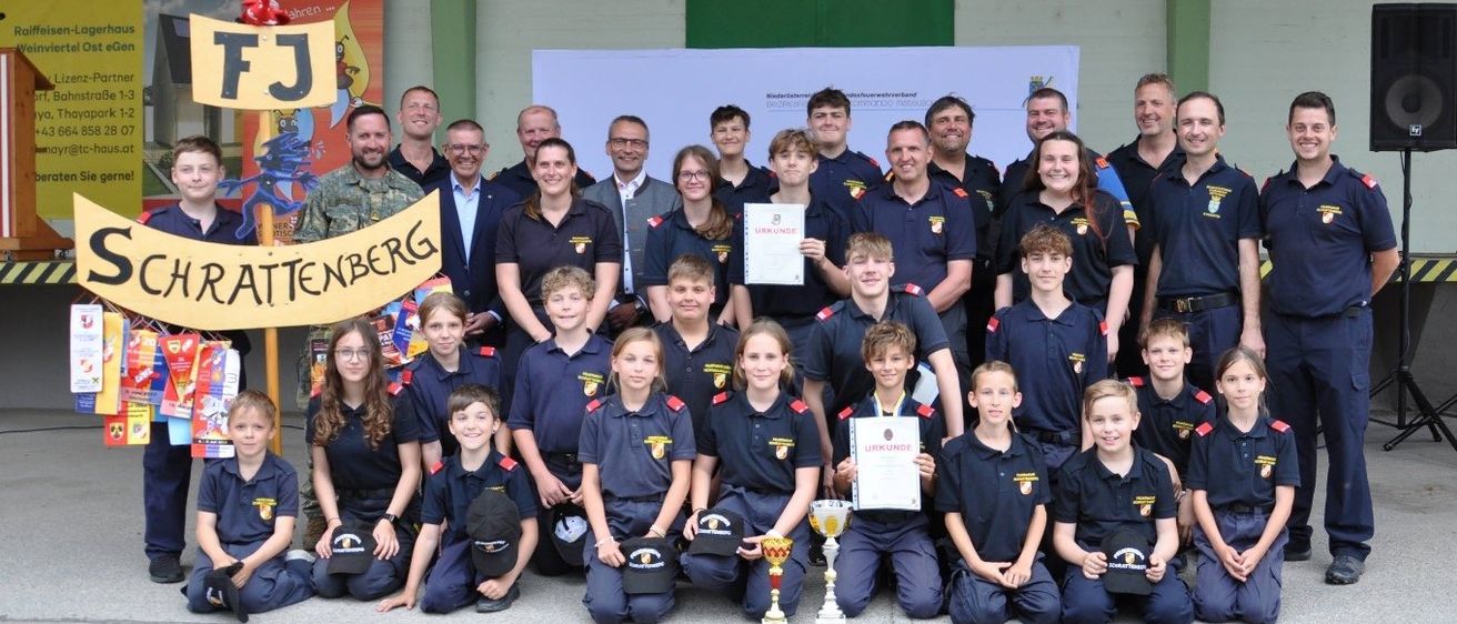 Eine Gruppe junger Menschen in blauen Uniformen mit einigen Erwachsenen posiert für ein Foto mit Trophäen und Urkunden. Sie stehen auf einer Betonfläche.