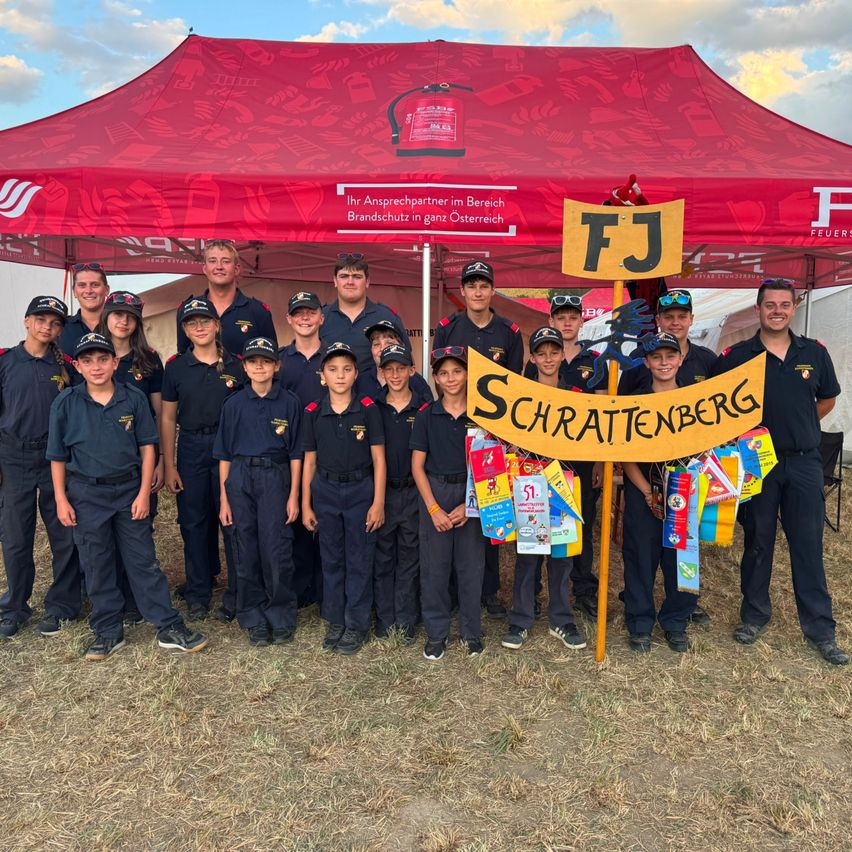Eine Gruppe junger Menschen in Uniform, die unter einem roten Zelt mit einem Banner mit der Aufschrift Schrattenberg stehen. Sie halten ein gelbes Banner mit den Buchstaben FJ und der Nummer 51.