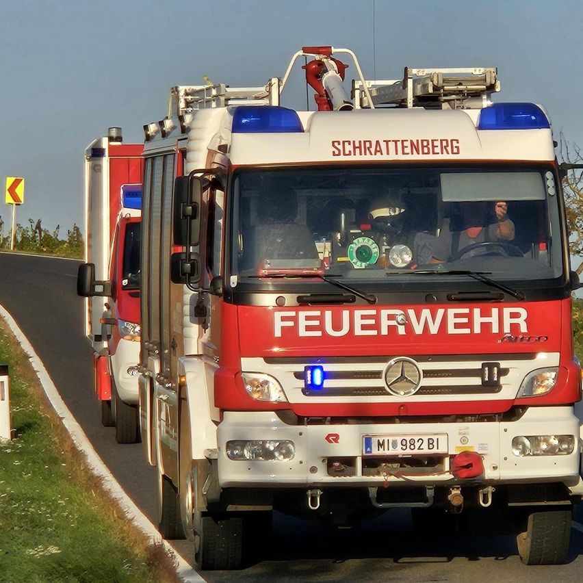 Ein roter Feuerwehrwagen mit dem Wort 'FEUERWEHR' auf der Front fährt eine Straße entlang.