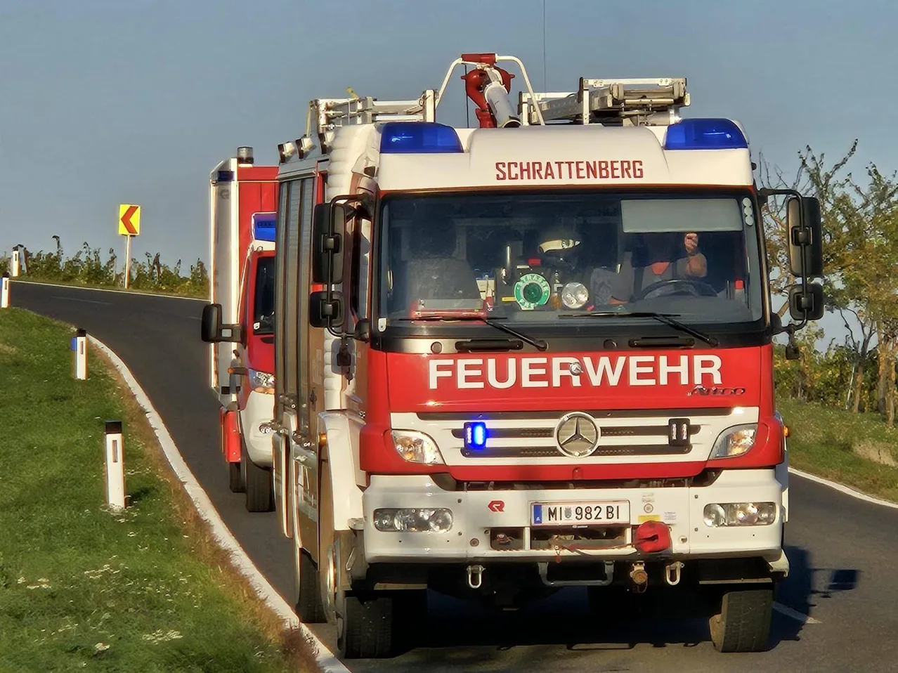 Ein roter Feuerwehrwagen mit dem Wort 'FEUERWEHR' auf der Front fährt eine Straße entlang.