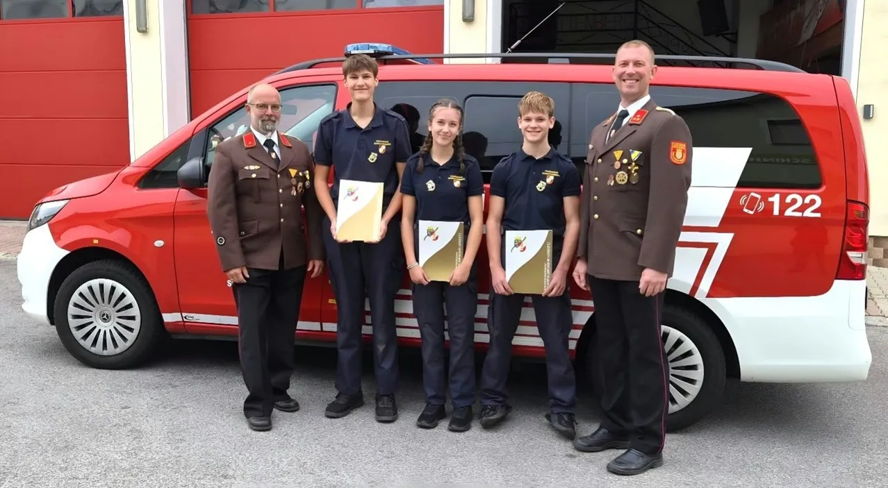 Fünf Personen stehen vor einem roten und weißen Van, möglicherweise einem Feuerwehrwagen. Sie sind alle in Uniform gekleidet und halten jeweils ein Zertifikat.