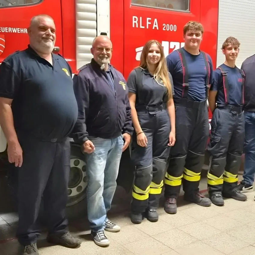 Eine Gruppe von Menschen, wahrscheinlich Feuerwehrleute, steht vor einem Feuerwehrauto.