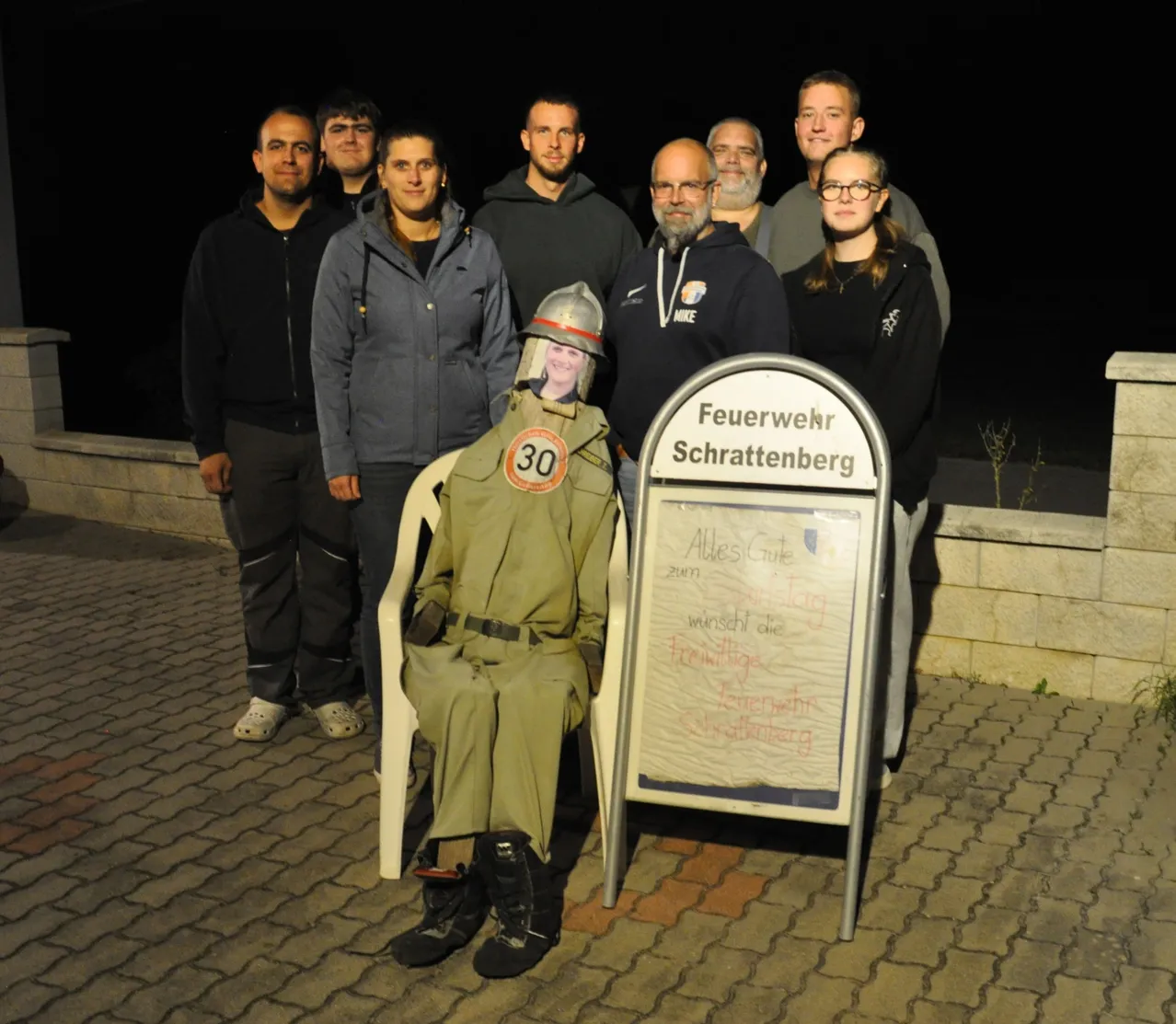 Eine Gruppe von Menschen posiert nachts für ein Foto. Eine Person ist als Feuerwehrmann verkleidet.