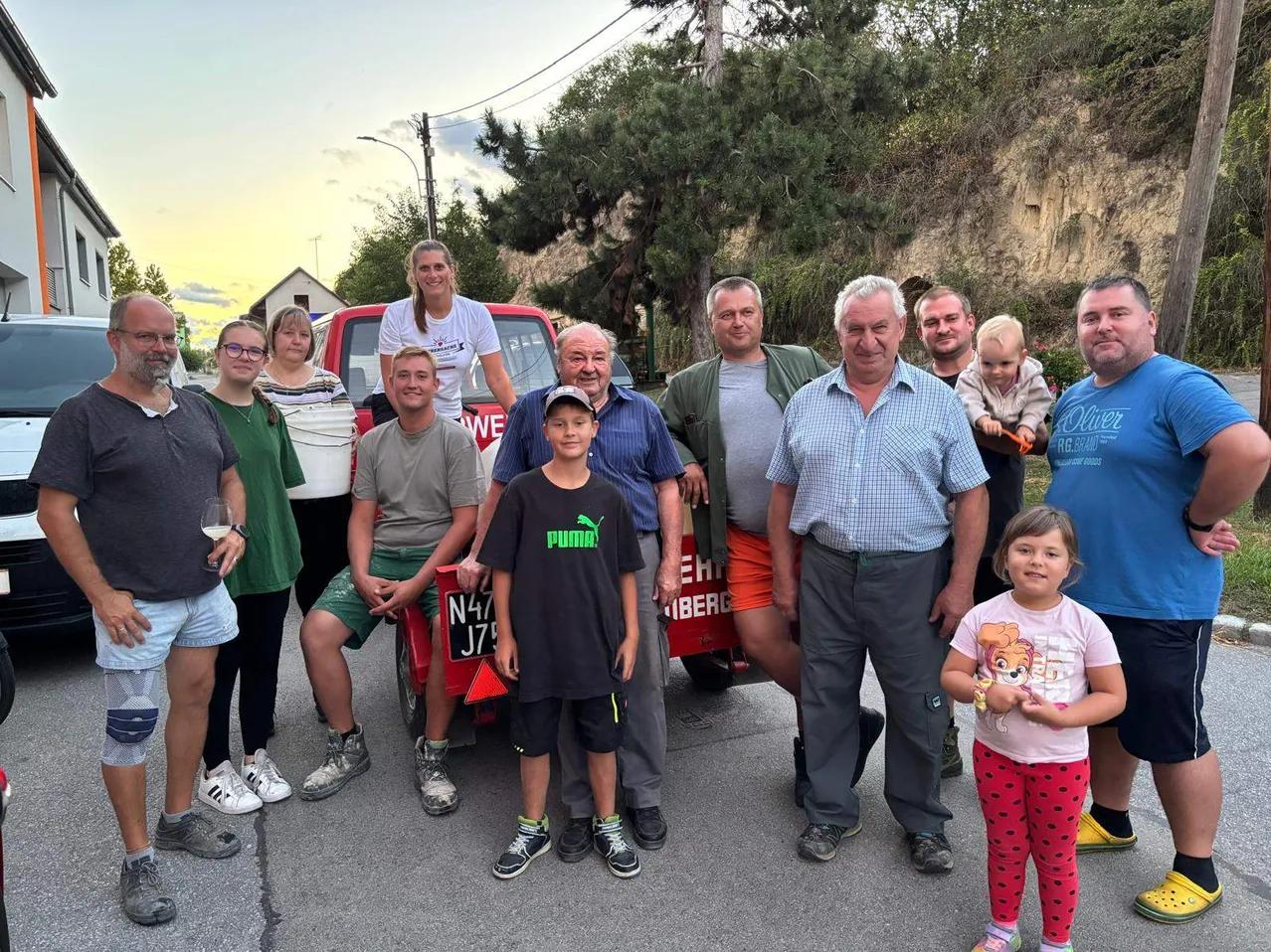 Eine Gruppe von Menschen steht vor einem roten Pickup-Truck. Sie alle lächeln und scheinen für ein Foto zu posieren.