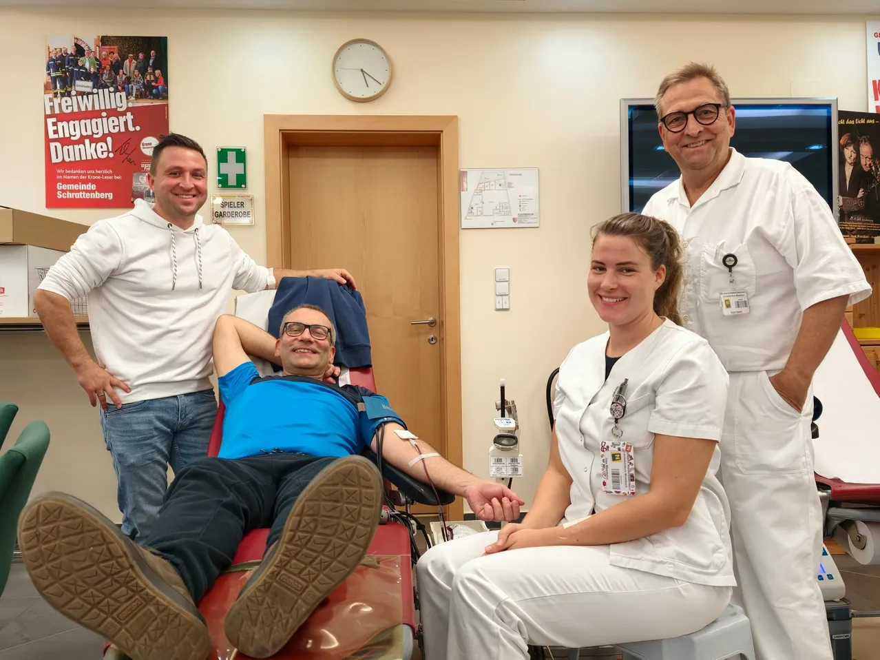 Ein Mann liegt auf einem roten Stuhl und lächelt, während eine Frau in weißer Uniform ihm Blut abnimmt.