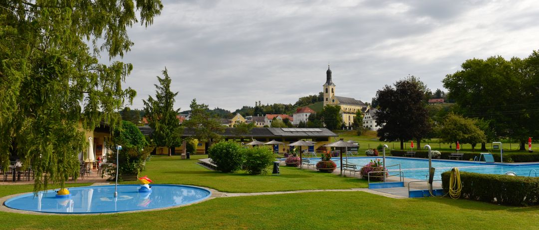 Ein ruhiger Außenpoolbereich mit saftigem grünem Gras und einer Kirche im Hintergrund, unter einem bewölkten Himmel.
