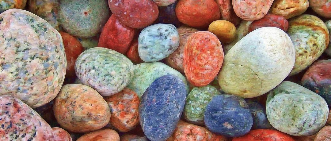 Eine Sammlung von leuchtenden, farbenfrohen Steinen, in verschiedenen Rottönen, Orange, Gelb, Blau, Grün und Weiß bemalt, ist in einem Haufen angeordnet. Die Steine zeigen einzigartige Texturen und Muster.