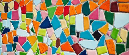 Ein farbenfrohes Mosaik aus bunten Kacheln in verschiedenen Formen und Größen, das ein komplexes Muster auf einer Betonoberfläche bildet.