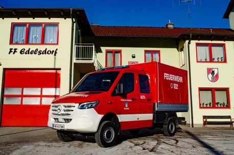 Ein rot-weißer Mercedes-Benz-Notfallfahrzeug steht vor einem Gebäude mit rotem Dach und roten Garagentoren.