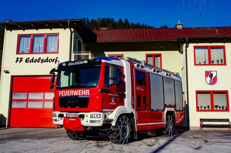 Ein roter Feuerwehrwagen aus der Gemeinde Edelsdorf ist vor einem Gebäude geparkt. Das Gebäude hat ein rotes Dach und rote Fenster.
