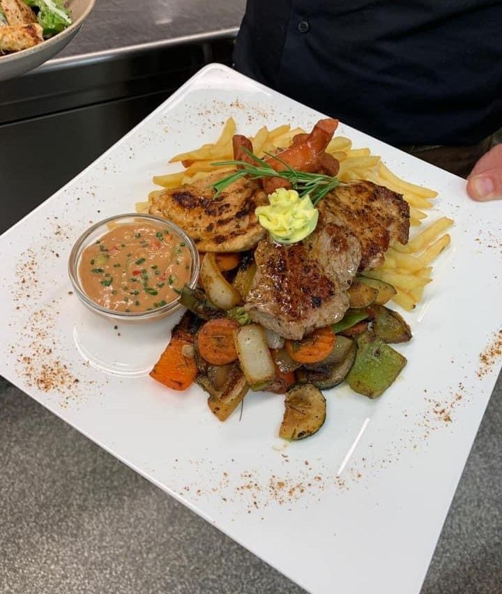 Ein Teller mit gegrilltem Hähnchen, Steak und Gemüse mit einer Beilage Pommes und einer Dip-Sauce.