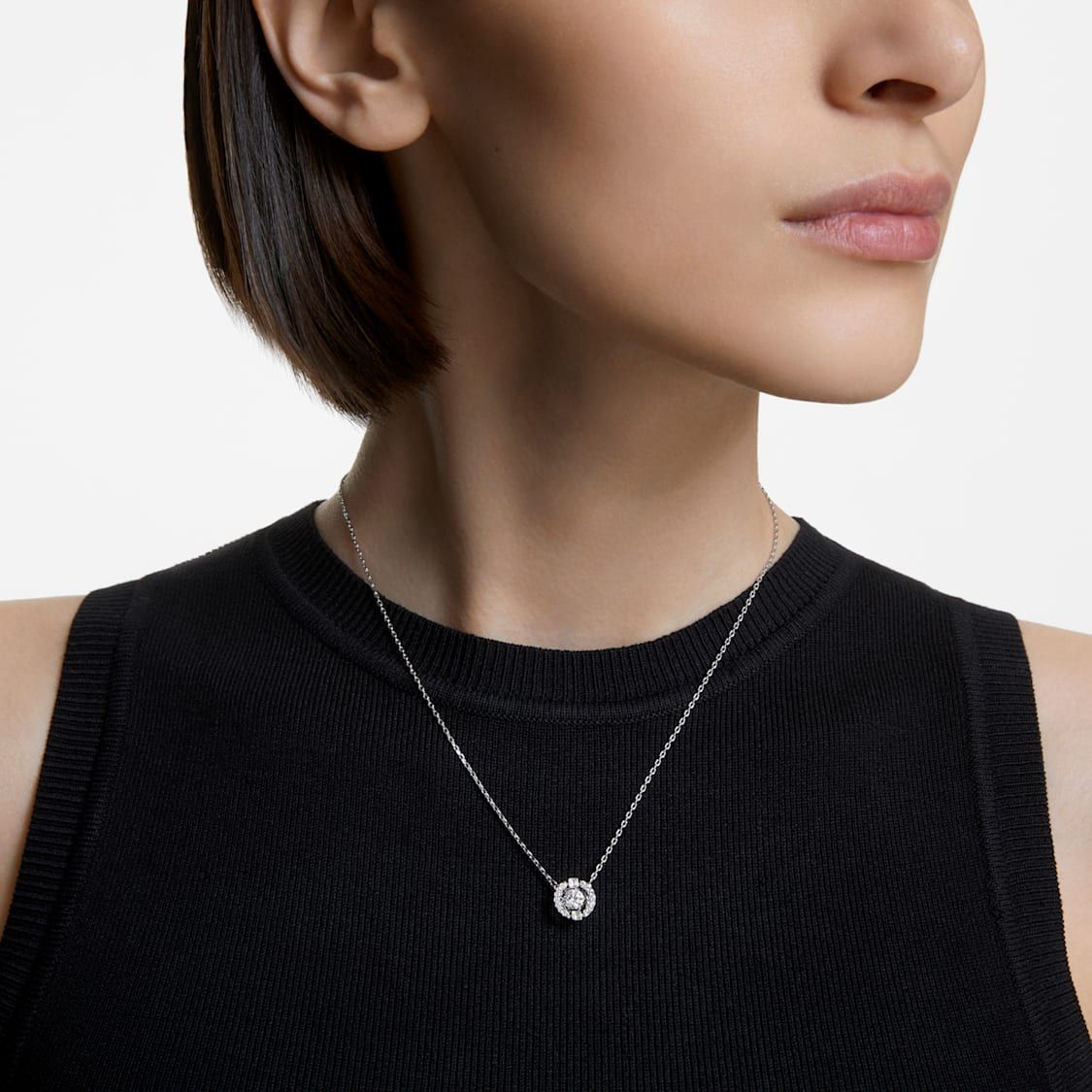 A woman with short hair is wearing a silver necklace with a diamond pendant. She is dressed in a black sleeveless top.