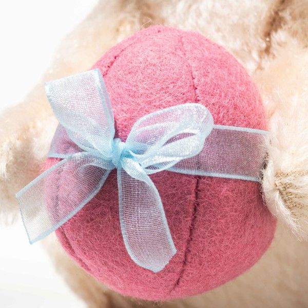 Ein Nahaufnahme eines rosa, filzierten Balls mit einer blauen Schleife darum. Die Schleife ist in einem Bogen am Ball gebunden, der wie ein Plüschtier erscheint.