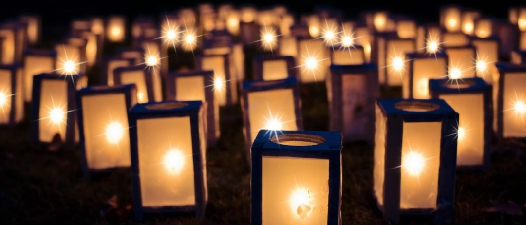Viele beleuchtete Laternen sind nachts im Kreis auf dem Boden aufgestellt. Jede Laterne gibt ein warmes, helles Licht ab.