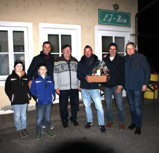 Sieben Männer und Jungen stehen nachts vor dem Gebäude des LFJ Helm und lächeln für ein Foto. Ein Mann hält eine Geschenkbox.