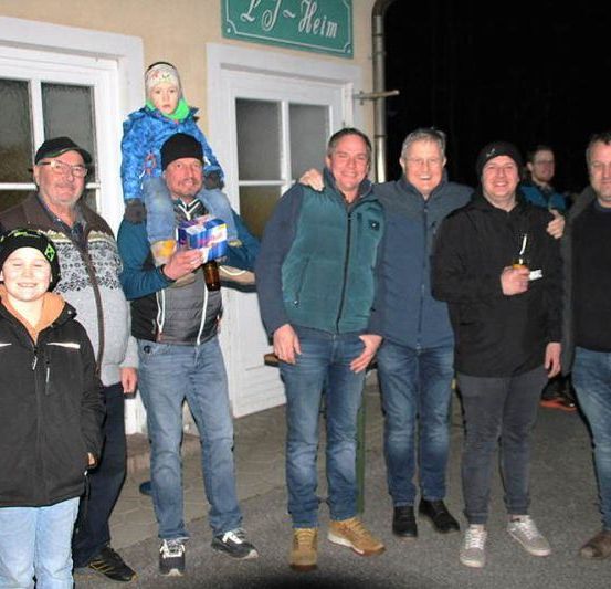 Eine Gruppe von Männern und Jungen, einer trägt ein Kind, steht vor einem Gebäude mit einem Schild, das Lof Heim liest.
