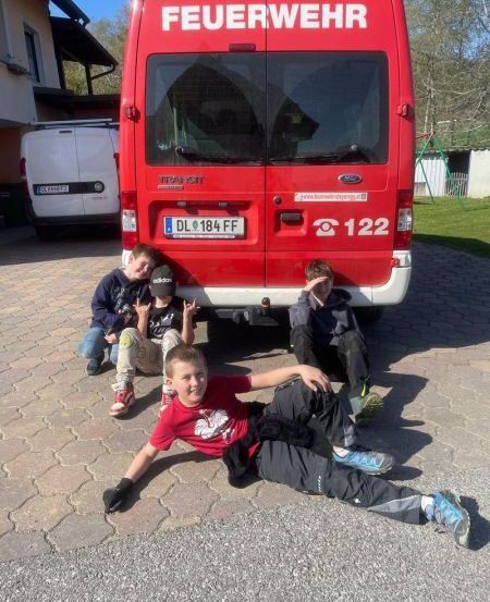 Vier junge Jungen posieren für ein Foto vor einem roten Feuerwehr-Van mit dem Kennzeichen DL 184 FF.