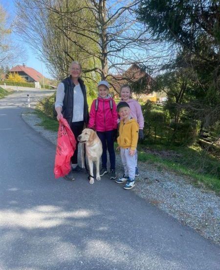 Eine Familie mit einem Hund steht auf einem Schotterweg und lächelt für ein Foto. Der Hund trägt eine Leine.