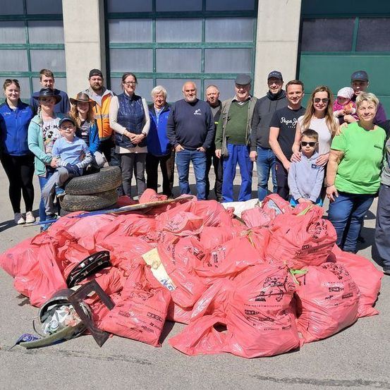 Eine Gruppe von Menschen, einschließlich Erwachsener und Kinder, steht draußen und posiert für ein Foto vor einem Gebäude. Es gibt mehrere rote Plastiktüten mit Müll auf dem Boden.