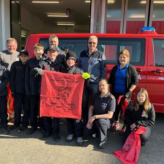 Eine Gruppe von Menschen in Uniformen posiert für ein Foto vor einem roten Feuerwehrwagen. Der Feuerwehrwagen hat die Aufschriften Freiwillige Feuerwehr und Wielfrensen.