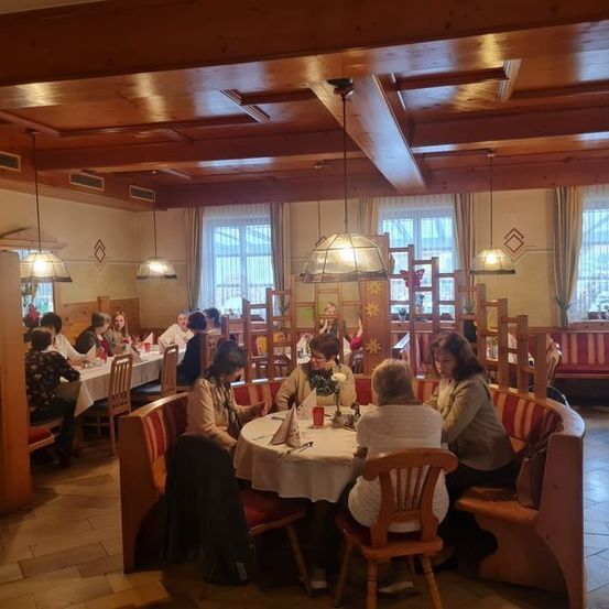 Ein Restaurant mit Holztischen und Stühlen. Mehrere Frauen sitzen und unterhalten sich. An der Decke hängen Lampen.