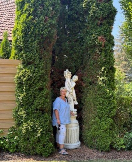 Eine Frau steht neben einer Statue in einem Garten mit Hecken.