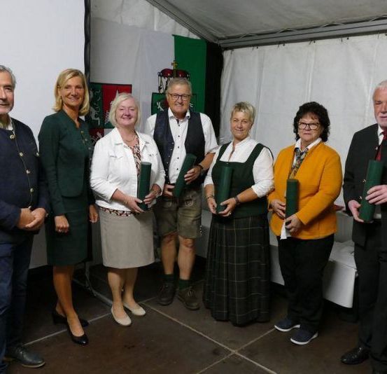 Eine Gruppe von Menschen, sowohl Männer als auch Frauen, stehen in einem Zelt und halten grüne Gegenstände. Sie alle lächeln und scheinen für ein Foto zu posieren. Sie tragen formelle Kleidung. Hinter ihnen ist eine weiße Wand mit einem grünen Banner.