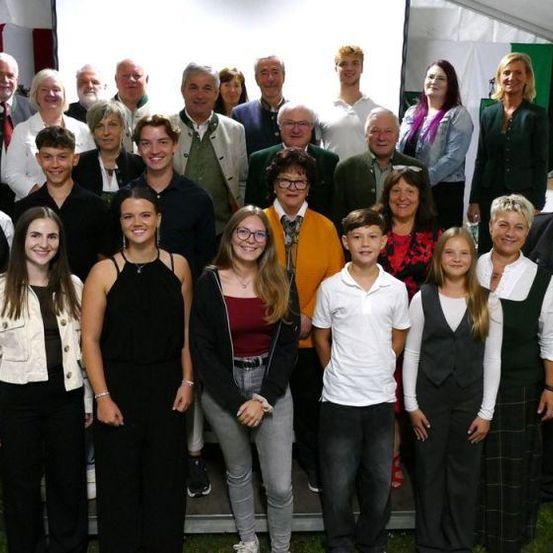 Eine große Gruppe von Menschen posiert für ein Foto, einige in formeller Kleidung und andere in lässiger Kleidung, vor einem Zelt mit einer Europaflagge.