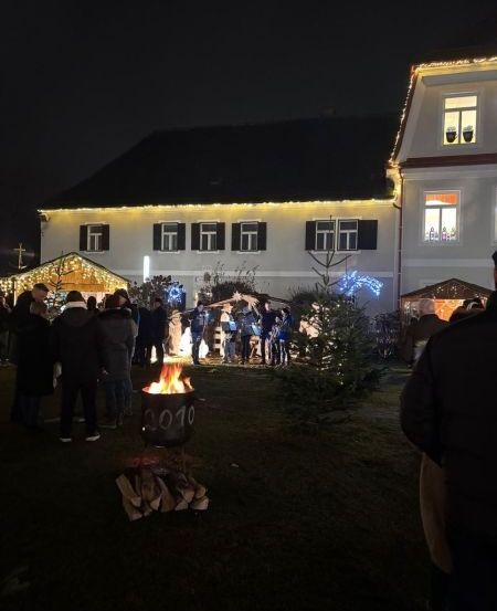 Eine Gruppe von Menschen versammelt sich um ein Lagerfeuer vor einem dekorierten Haus bei Nacht.