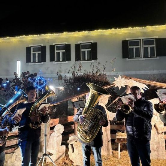Eine Gruppe von Männern spielt Blechblasinstrumente vor einem dekorierten Gebäude in der Nacht.